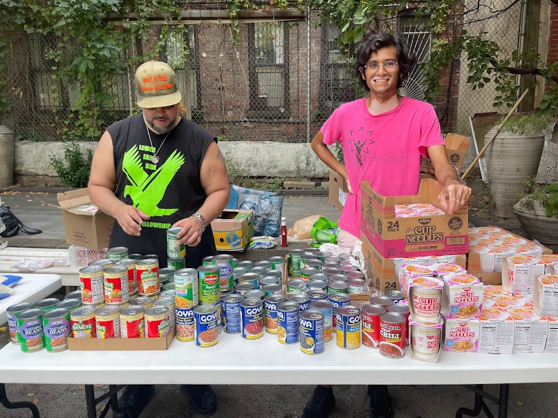 Volunteers standing behind canned goods and noodles at a distribution table